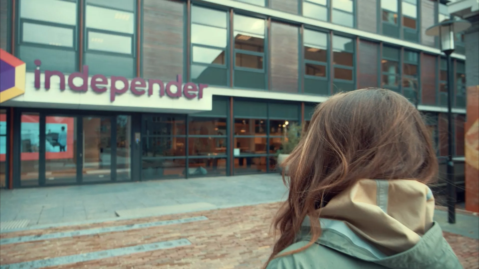 Jonge vrouw loopt richting het moderne gebouw van Independer in Hillywood onderstreept de dynamische en inspirerende werkomgeving